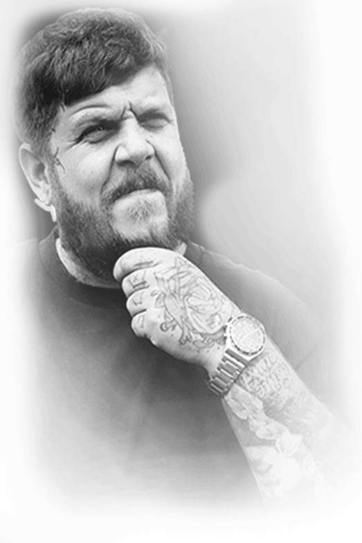 Tätowierer Wien Rares - Porträt Tätowierer Rares mit Bart, die tätowierte Hand am Kinn und Uhr am Handgelenk, Schwarz-Weiß-Porträt, Ink21 Tattoo Studio Wien
