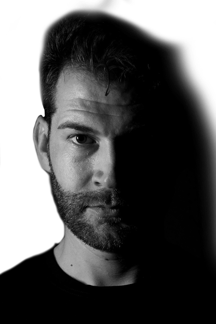 Tätowierer Wien Tibi - Porträt Porträt von Tätowierer Tibi mit Bart, eine Gesichtshälfte im Schatten, Schwarz-Weiß-Foto, Ink21 Tattoo Studio Wien