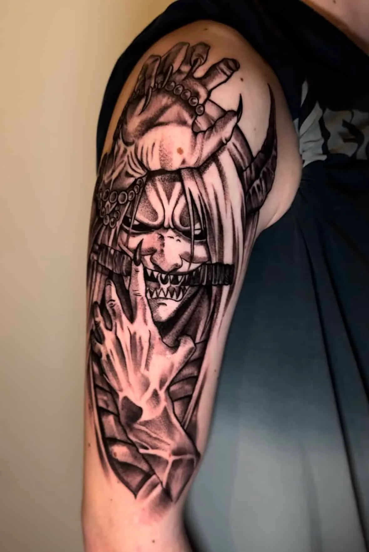 Blackwork Tattoo einer japanischen Oni-Dämonenmaske mit Hörnern und Krallenhänden am Oberarm, Tattoo Studio Wien