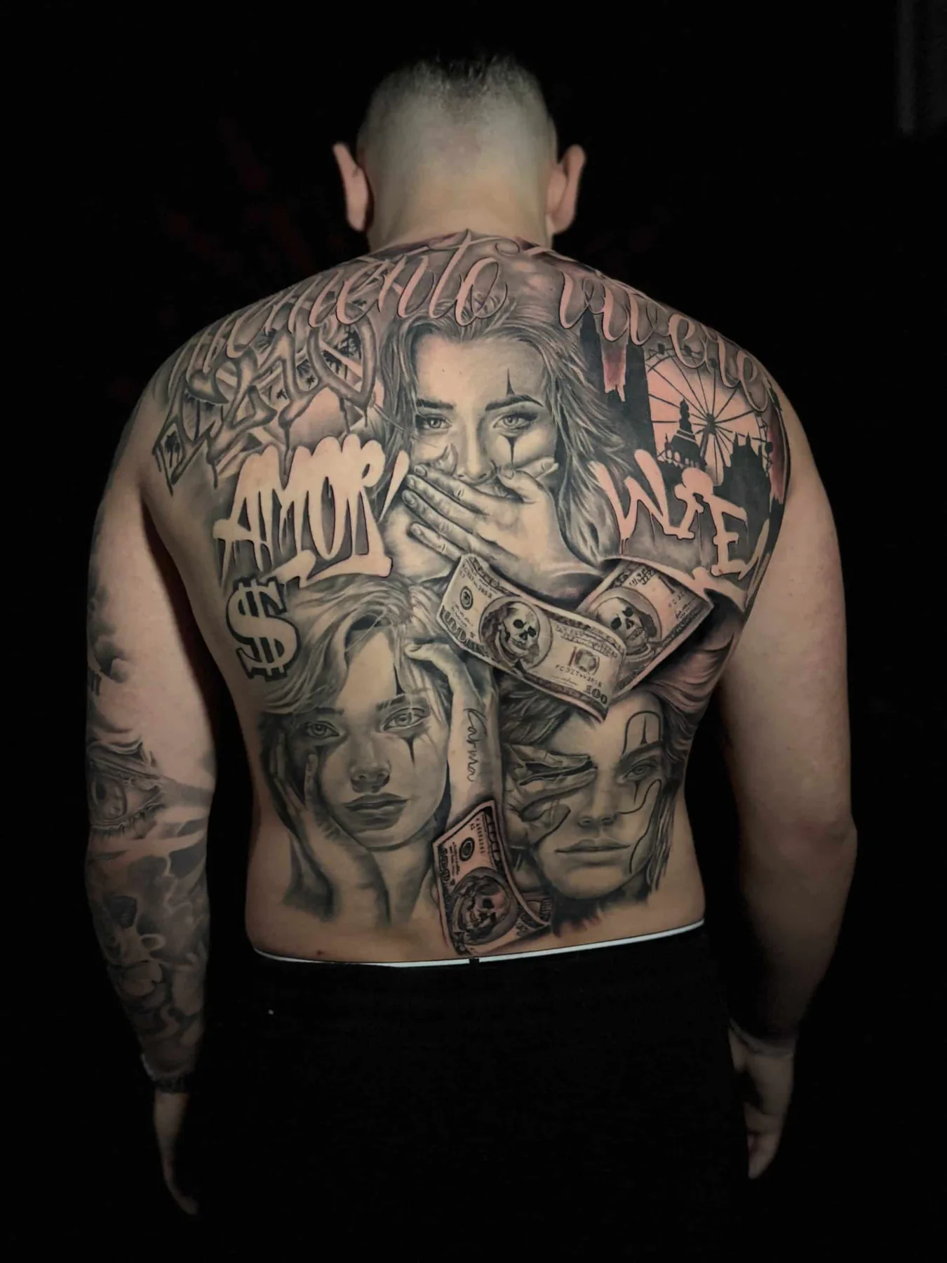 Chicano Rückentattoo in Black & Grey mit Clown-Frauengesichtern, Geldscheinen, Schriftzug „Amor“ und dem Wiener Riesenrad
