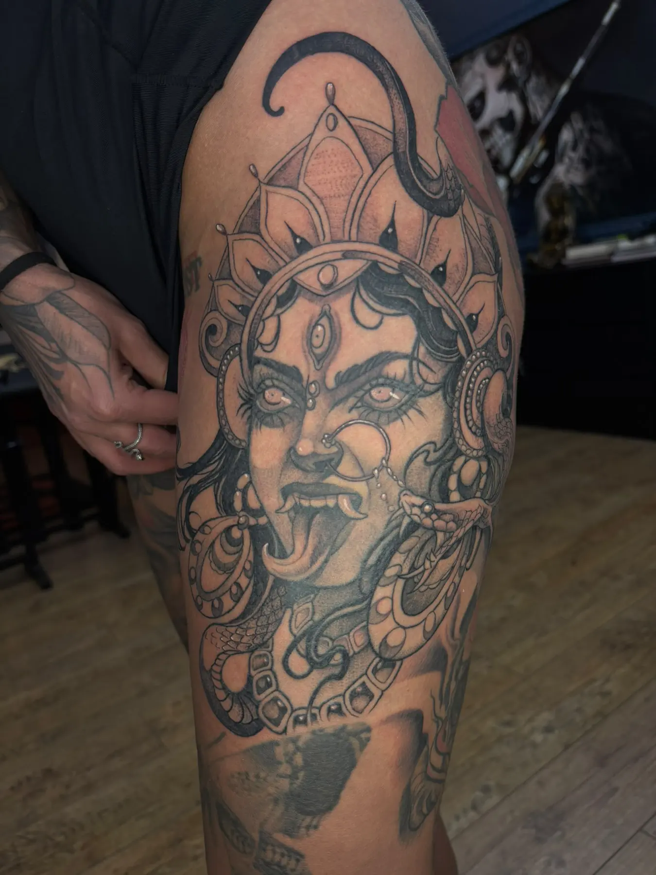 Illustratives Black & Grey Tattoo der Göttin Kali mit drittem Auge, Zunge, Schlangen und Krone am Oberschenkel, Wien