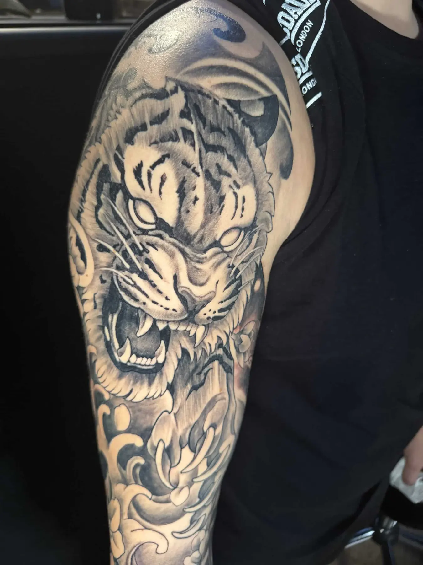 Japanisches Tattoo in Black & Grey: brüllender Tiger mit Chrysanthemen und Wellen am Oberarm und an der Schulter, Wien