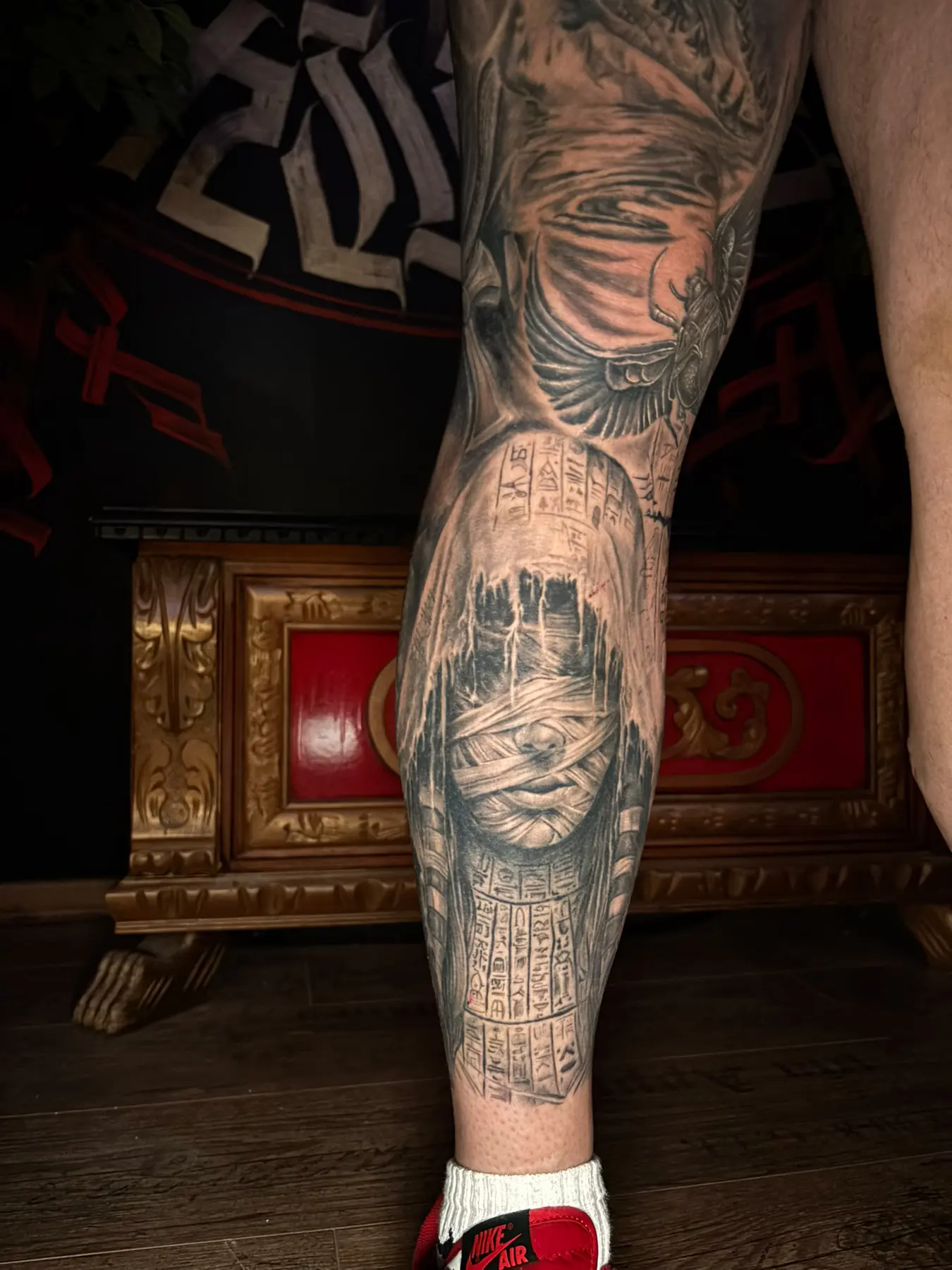 Black & Grey Tattoo an der Wade: Ägypterin mit Augenbinde, Hieroglyphen und geflügelter Skarabäus, Leg Sleeve Wien