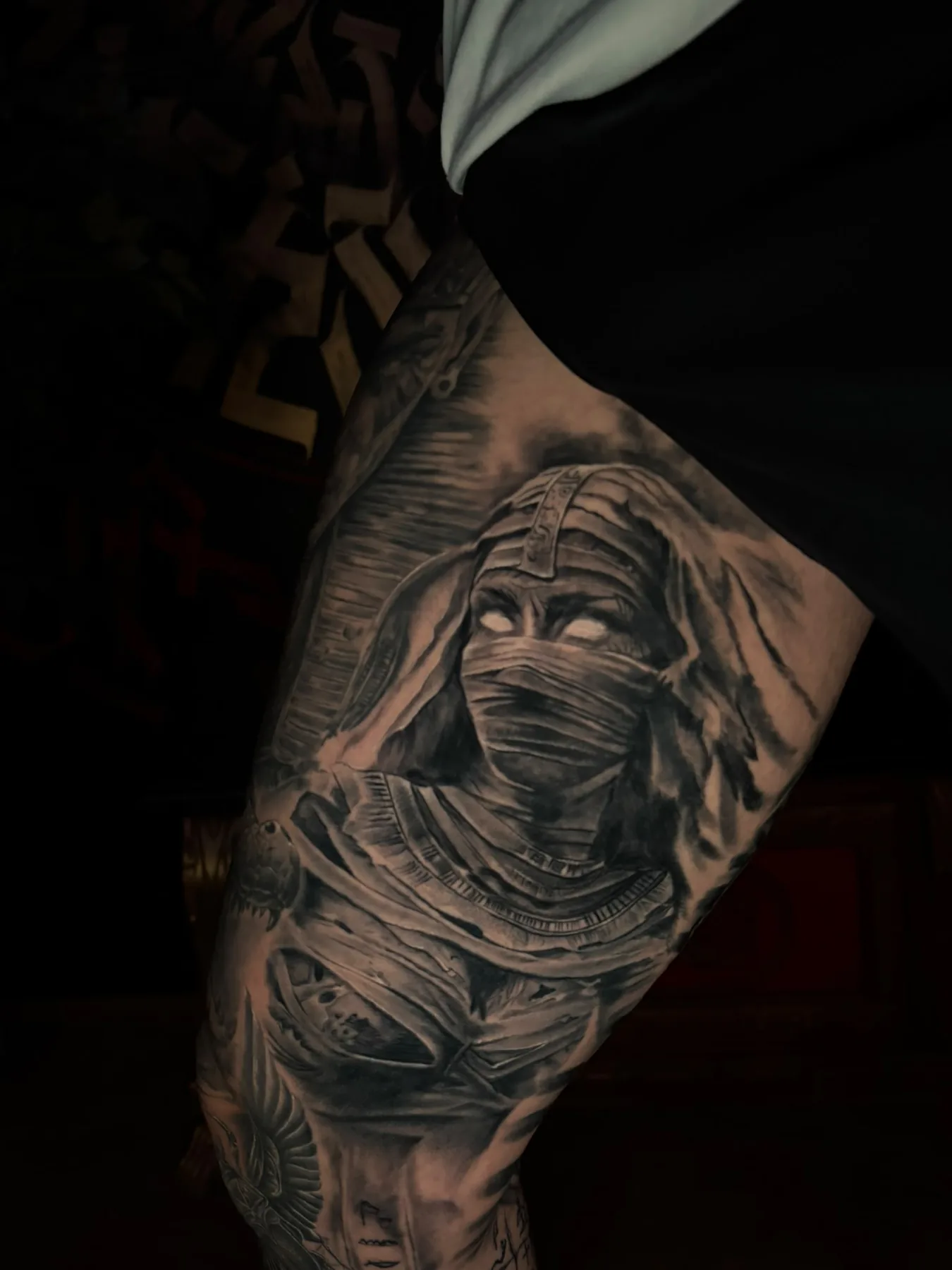 Black & Grey Realismus Tattoo: verhüllte Mumie mit weißen Augen am Oberschenkel, Teil eines ägyptischen Leg Sleeves, Wien