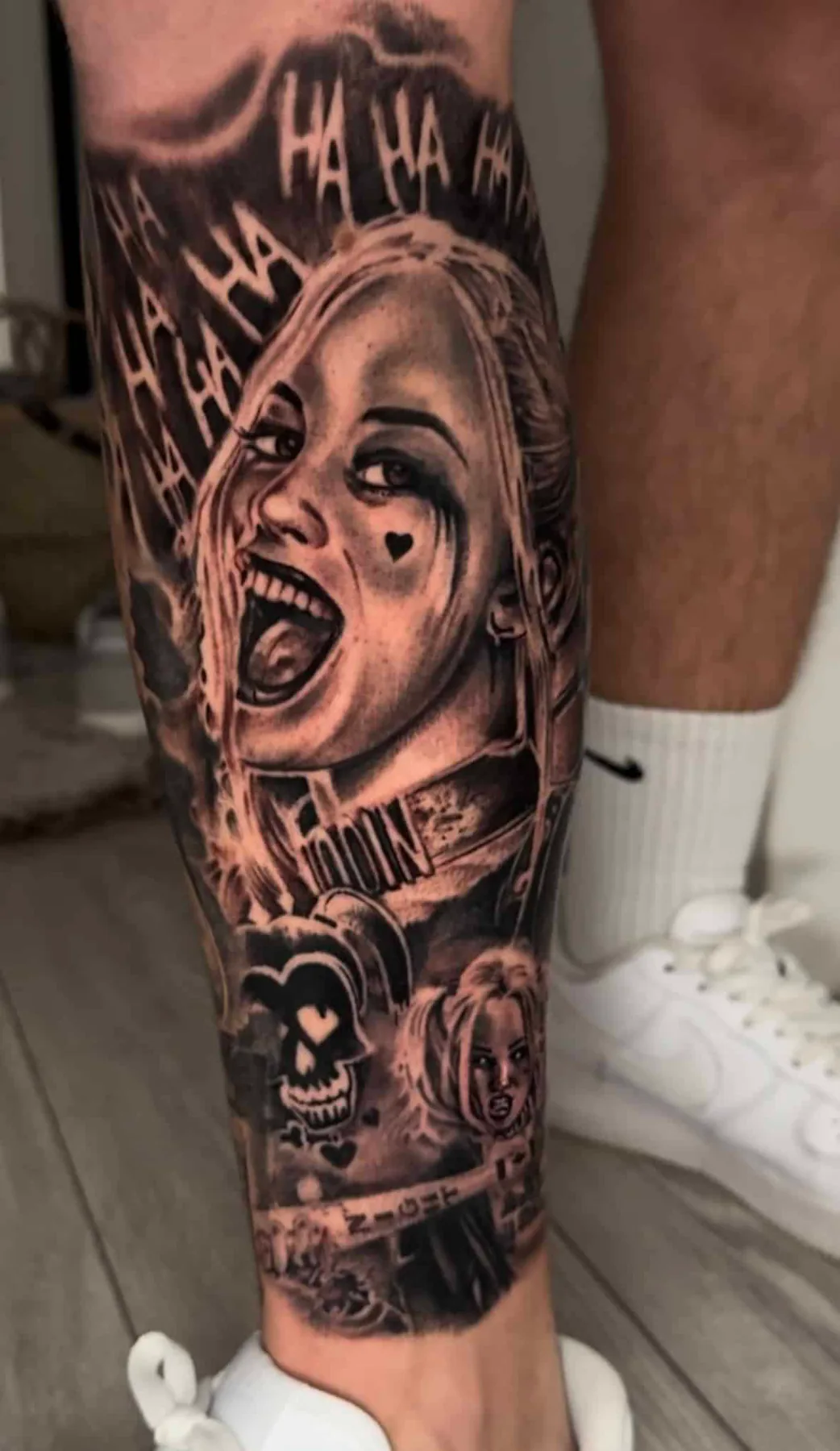 Realistisches Black & Grey Porträt von Harley Quinn, lachend mit „HA HA“-Schriftzug und Narren-Totenkopf an der Wade, Wien