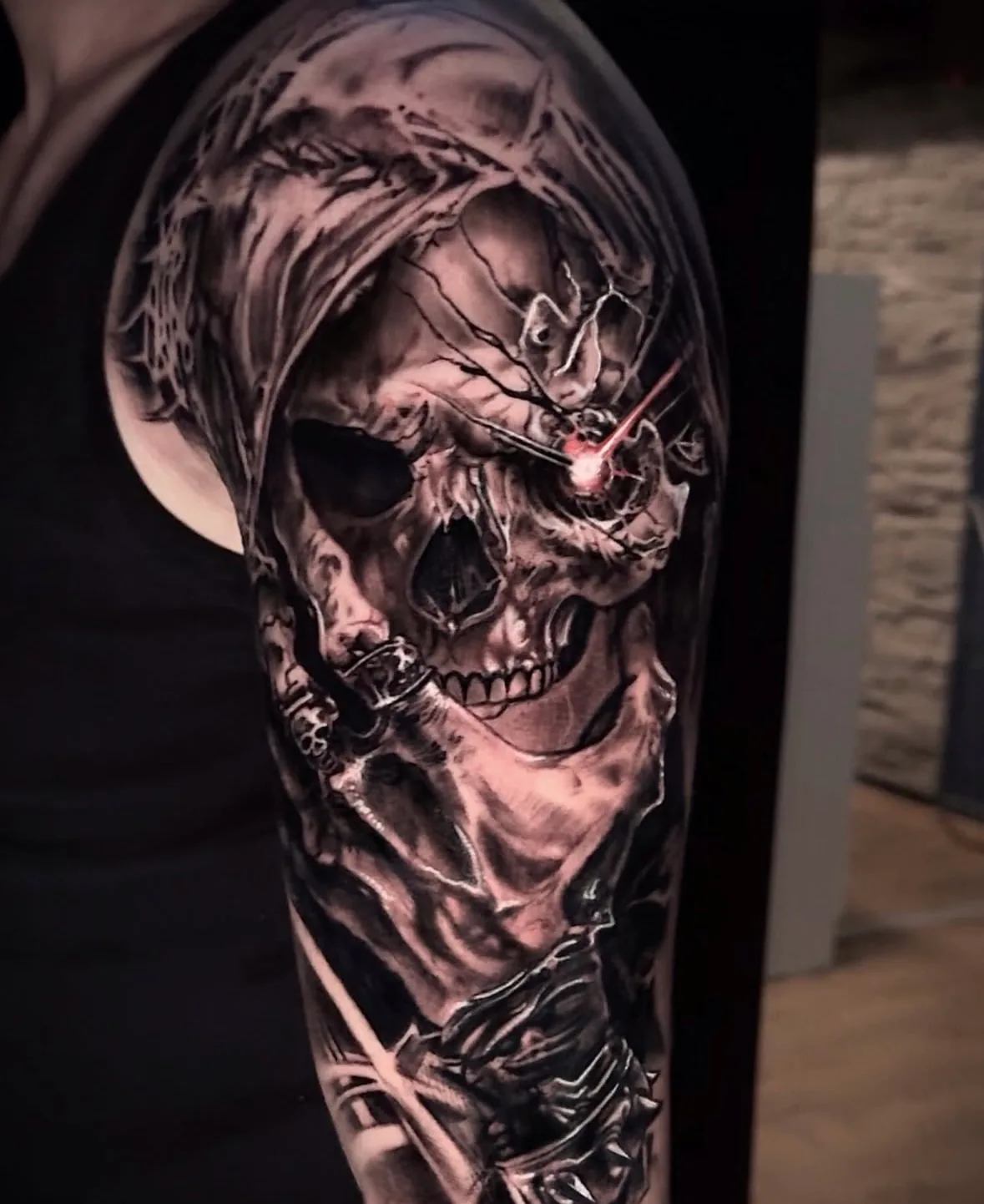 Horror Tattoo in Black & Grey: Sensenmann-Totenkopf mit Kapuze und rotem Lichtstrahl im Auge am Oberarm, Tattoo Wien