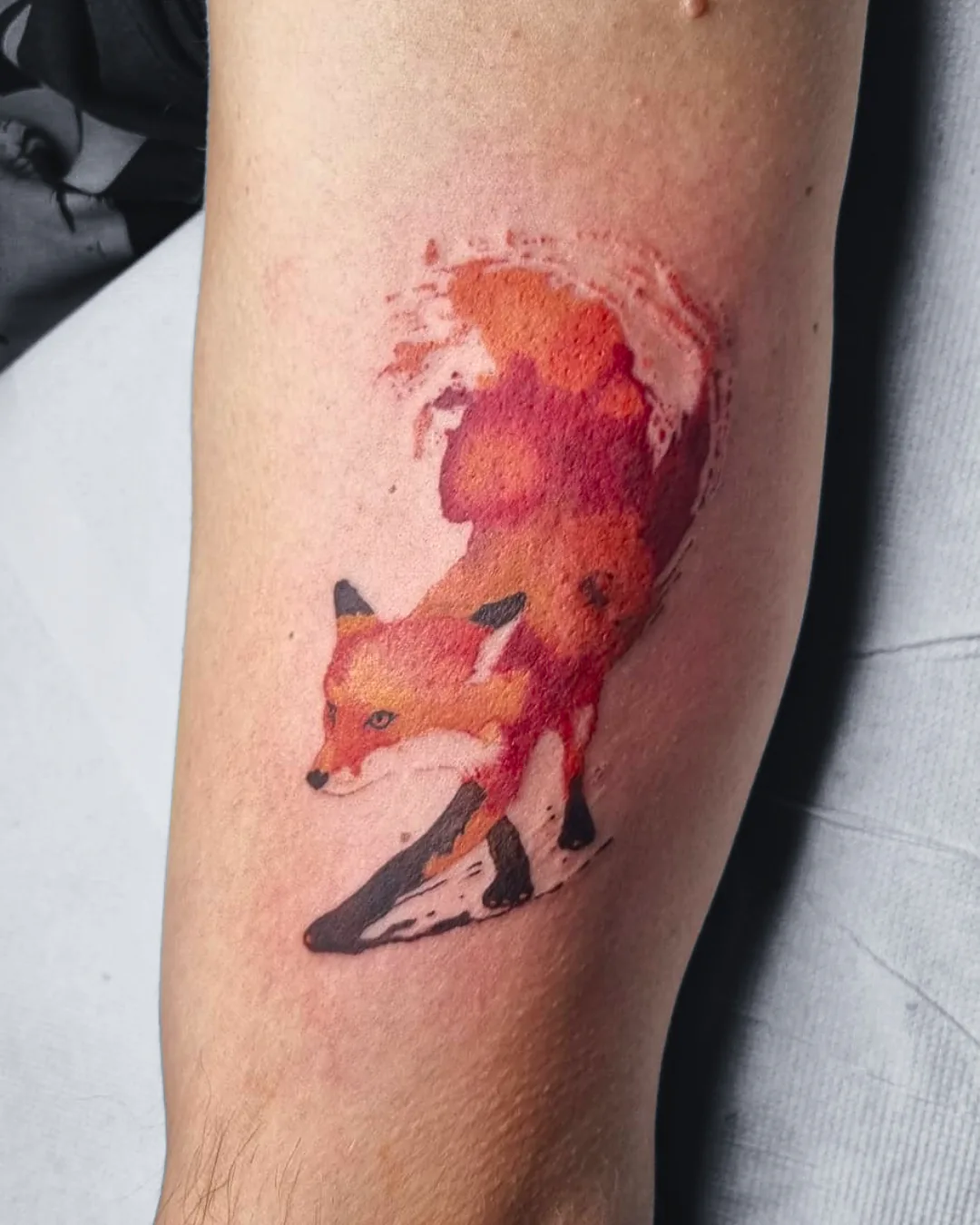 Watercolor Tattoo eines Fuchses in Orange- und Rottönen mit schwarzen Pfoten am Arm, Aquarell-Stil, Tattoo Studio Wien