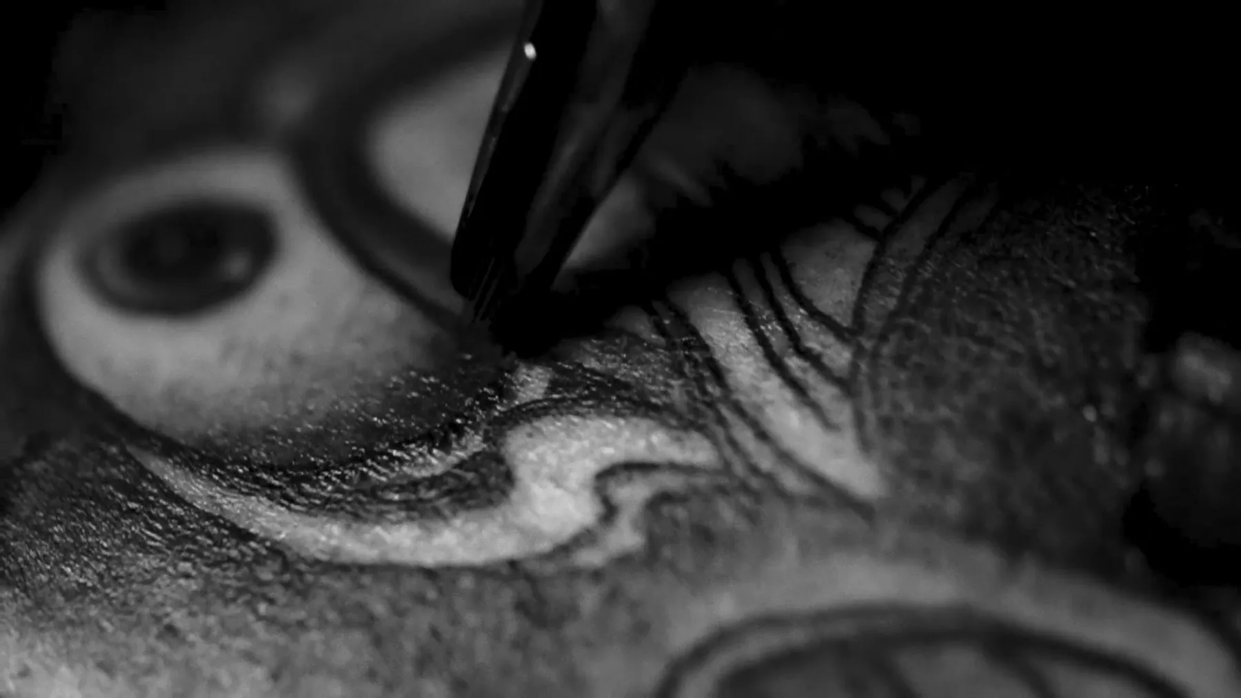 Tattoo-Nadel in Aktion - Tattoo Studio Wien Ink21 Nahaufnahme einer Tattoo-Nadel beim Schattieren eines Black & Grey Tattoos mit Auge und geschwungenen Linien, Tattoo Wien